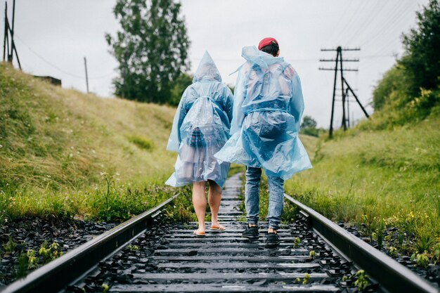 Reisende Paare in blauen Regenmänteln gehen entlang der Eisenbahn in der Natur
