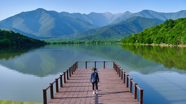 Reisender, der allein auf Pier steht und auf See und Berge starrt. Genießen Sie das schöne Freiheitsmoment und die ruhige, friedliche Atmosphäre in der Natur. Rückansicht