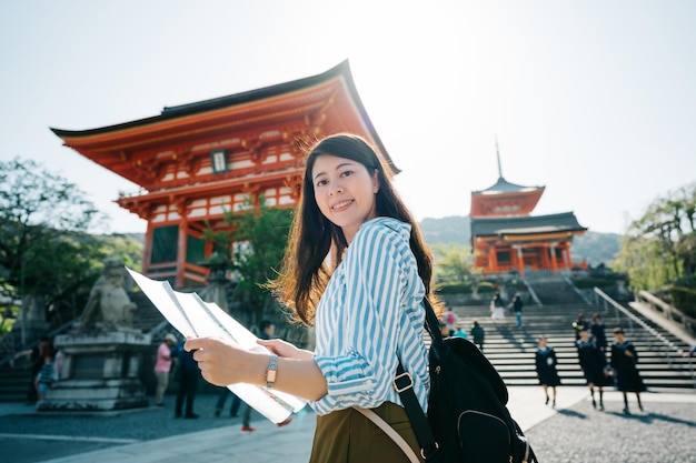 Foto reisender, der an der führerinformation liest, die vor dem japanischen tempel steht. gymnasiasten, die im hintergrund die treppe hinuntergehen. backpacker reisen allein in japan.