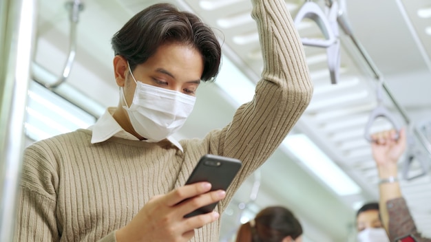 Reisender, der Gesichtsmaske trägt, während Handy im öffentlichen Zug benutzt