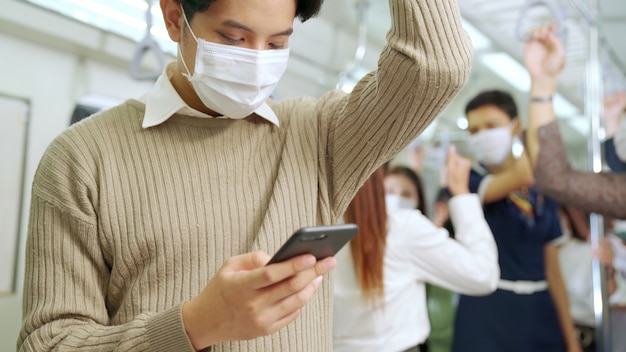 Reisender, die Gesichtsmaske tragen, während sie in öffentlichen Zügen ihr Mobiltelefon benutzen