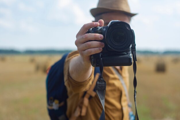 Reisender Fotograf mit einer Kamera in der Hand vor dem Hintergrund eines Feldes und Heuhaufen.