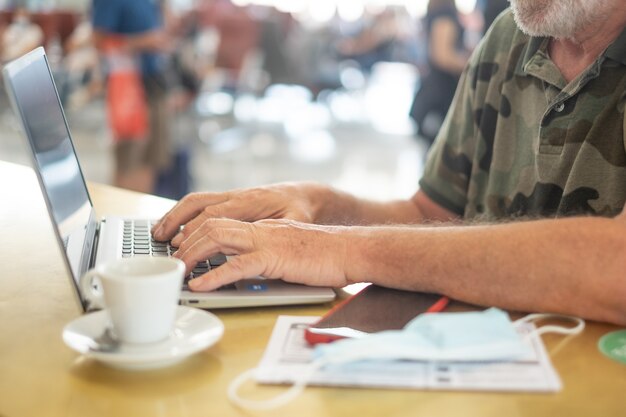 Reisender Mann am Flughafen, der auf das Boarding wartet, arbeitet an Laptop-Computer, Senior-Blogger-Remote-Arbeit, Hände auf Tastatur