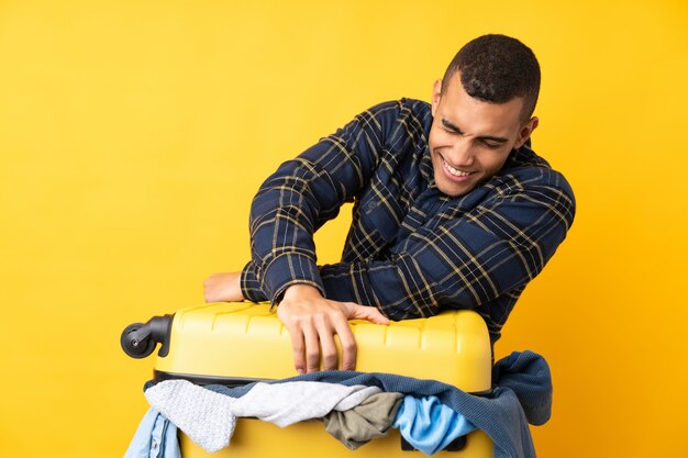 Reisender Mann mit einem Koffer voller Kleidung über isolierter gelber Wand