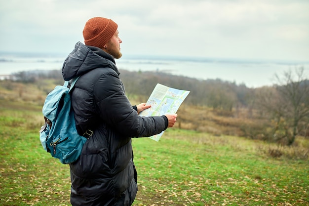 Reisender Mann mit Rucksack mit Karte in der Hand auf einer Wand des Gebirgsflusses der Natur, Reisekonzept, Urlaub und Lebensstilwanderkonzept