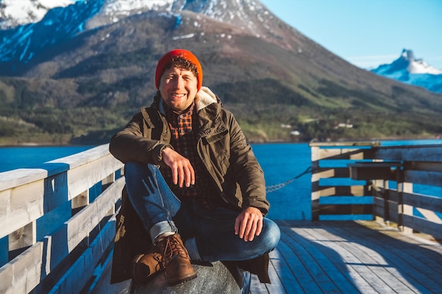 Reisender Mann sitzt auf einem Holzsteg auf einem Bergsee-Hintergrund Platz für Text oder Werbung