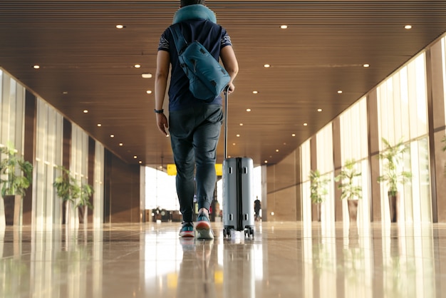 Reisender mit dem Koffer, der mit tragendem Gepäck und Passagier für Ausflug im Flughafenterminal geht