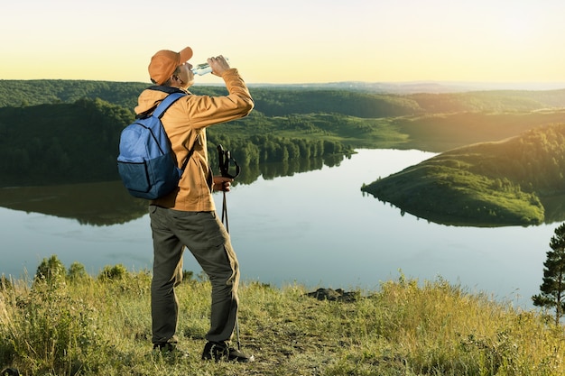 Reisender mit Rucksacktrinkwasser aus Plastikflasche in den Herbstbergen bei Sonnenuntergang. Aktiver, gesunder Lifestyle-Abenteuerreiseurlaub