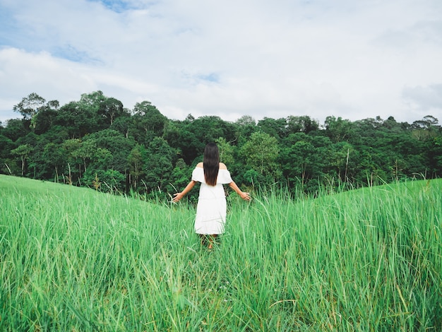 Reisendes Mädchen im weißen Kleid steht in Wiese und Wald und Berg mit Himmel und bewölktem Hintergrund