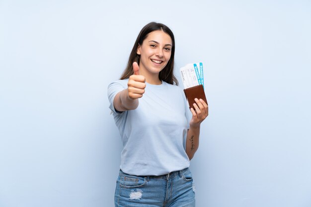 Reisendfrau mit Bordkarte über lokalisierter blauer Wand mit den Daumen oben, weil etwas Gutes geschehen ist