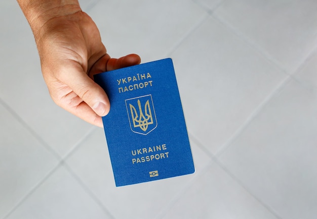 Reisepass eines Bürgers der Ukraine in männlicher Hand auf grauem Hintergrund, Nahaufnahme