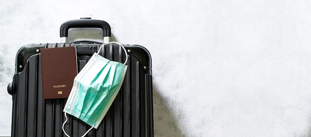 Reisetaschen und Maskenschwarzer Koffer mit Reisezubehör auf weißem Hintergrund Coronavirus 2019