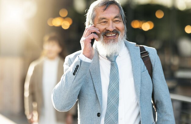 Reisetelefonanruf und Geschäftsmann, der mit einem Lächeln in der Stadt Bokeh spazieren geht, um Karrieremöglichkeiten zu kommunizieren oder erfolgreich zu verhandeln Urban Asian und Senior Boss oder Leader, die auf einem mobilen Smartphone sprechen