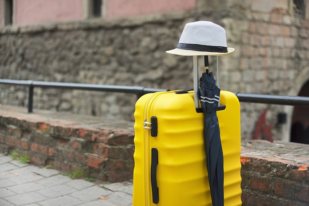 Reisetourismus-Konzept, gelber Plastikkoffer, Hut, Regenschirm