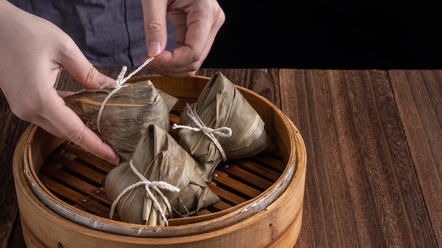 Reisknödel Zongzi Dragon Boat Festival Haufen chinesischer traditioneller gekochter Speisen im Dampfgarer auf Holztisch über schwarzem Hintergrund Nahaufnahme Kopierraum