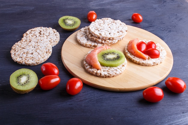 Reiskuchen mit Lachs-, Kiwi- und Kirschtomaten auf dunklem hölzernem Hintergrund.