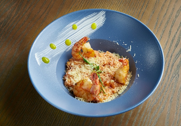 Reisrisotto mit Garnelen. Reis mit Meeresfrüchten in einer blauen Schüssel gegen ein Holz. italienische Küche