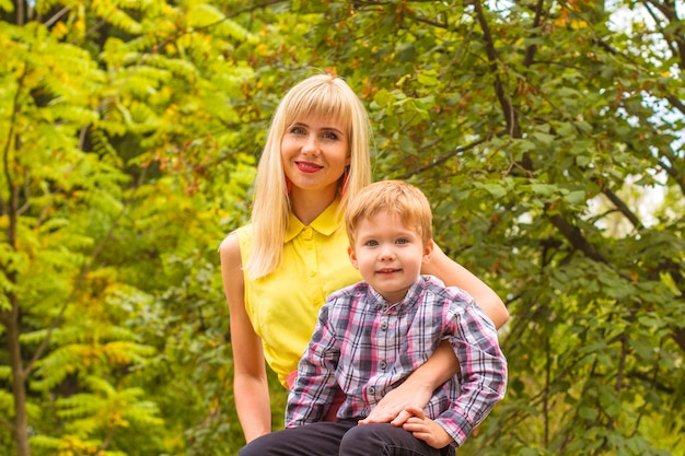 Reizend junge blonde Mutter, die ihren kleinen Sohn sitzt im Herbstpark umarmt