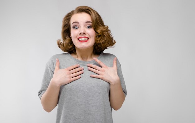 Reizend junges Mädchen in einem grauen T-Shirt auf einem grauen Hintergrund. Das Mädchen lehnte die Hände an die Brust