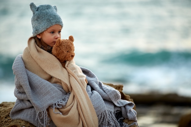 Reizend Mädchen mit dem Teddybären, der in Plaid streichelt