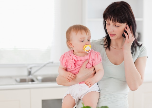 Reizende Frau am Telefon beim Anhalten ihres Babys in ihren Armen