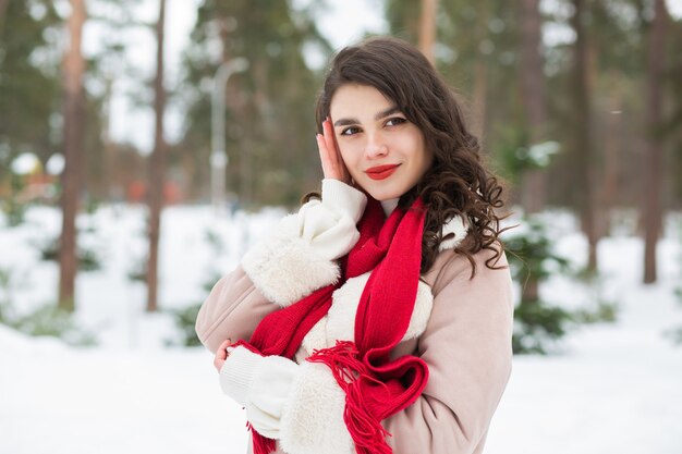 Reizende Frau mit rotem Lippenstift, die im verschneiten Winter aufwirft. Freiraum