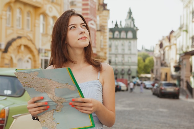 Reizende gehende Stadtstraßen der jungen Frau mit einer Karte