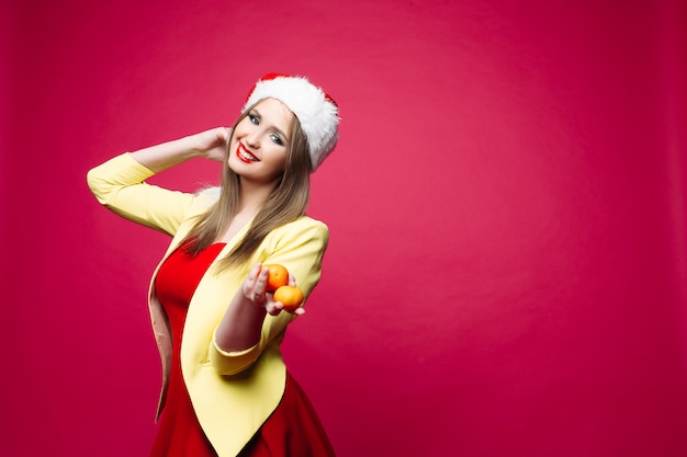 Reizende lächelnde Frau im festlichen Kleid und im Sankt-Hut mit Mandarinen.