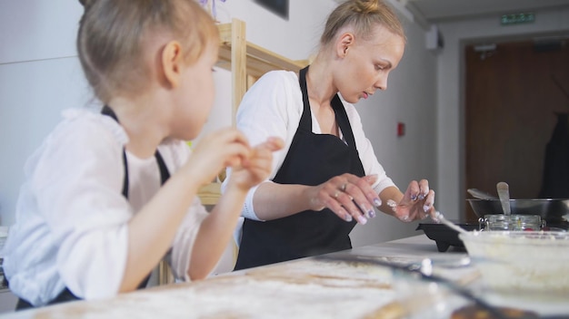 Reizende Mutter und kleine Tochter, die zusammen Pfannkuchen kochen