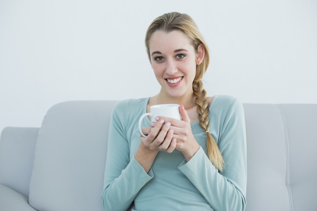 Reizende zufällige Frau, die eine Schale sitzt auf Couch hält