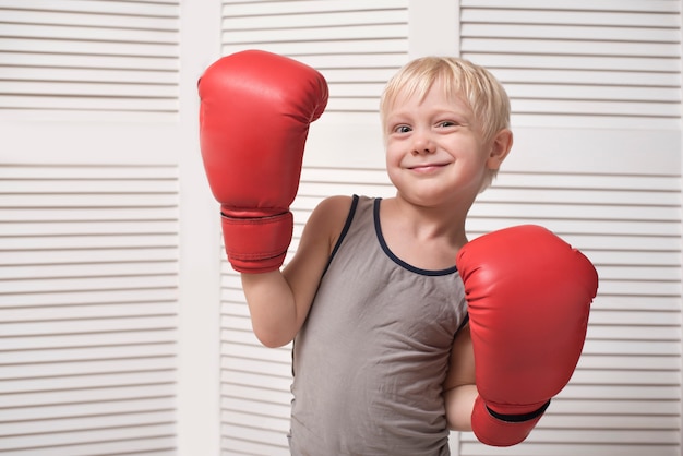 Reizender blonder Junge in den roten Boxhandschuhen. Sport-Konzept