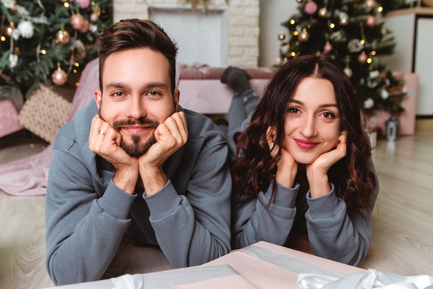 Reizendes junges romantisches Paar, das offene Geschenke sitzt, präsentiert Girlanden nach Hause gemütliche Innenatmosphäre