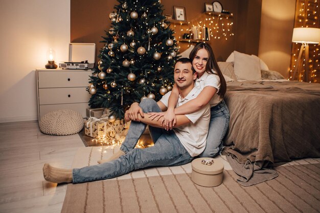 Reizendes junges romantisches Paar, das offene Geschenke sitzt, präsentiert Girlanden nach Hause gemütliche Innenatmosphäre