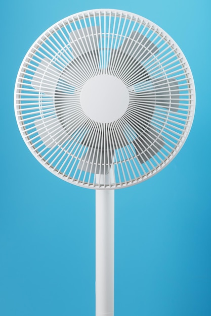 La rejilla y las aspas del ventilador eléctrico son blancas sobre fondo azul. Estilo minimalista, primer plano