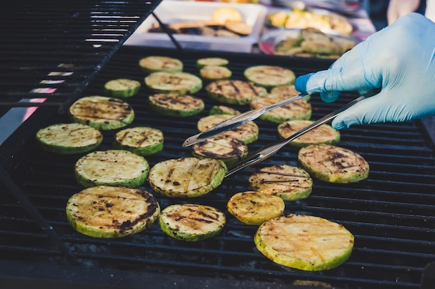 Rejilla de parrilla de contraste con calabacín frito Cocinar con un guante limpio voltea hacia el otro lado del calabacín frito El proceso de cocinar verduras a la parrilla