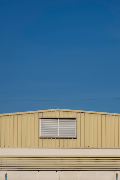 Rejillas de aluminio en la pared del almacén de acero amarillo contra el cielo azul claro en un estilo mínimo