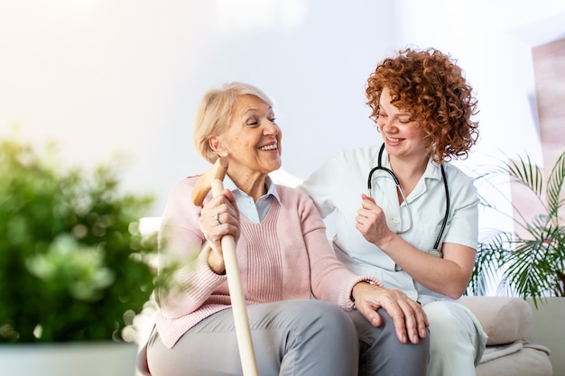 Relação amigável entre o cuidador sorridente em uniforme e feliz mulher idosa. Suporte jovem enfermeira olhando mulher sênior.