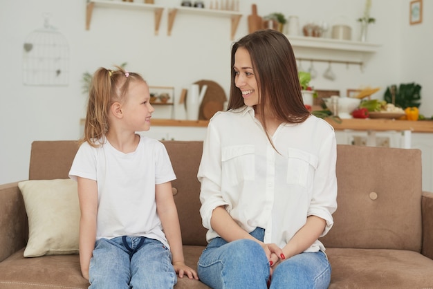 La relación de confianza de mamá e hija. Conversación de una mujer con una niña en su casa en el sofá de la cocina. Mejores amigos feliz fin de semana de maternidad junto con el concepto de niño.