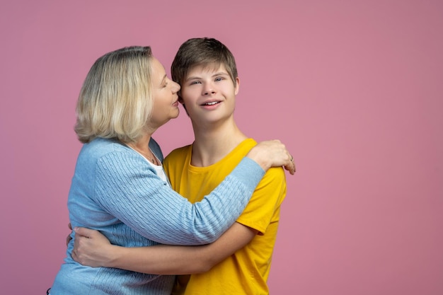 Relación de confianza. Una mujer de mediana edad que se preocupa abrazando su oído hablando atentamente escuchando a su hijo con síndrome de down de pie contra un fondo claro