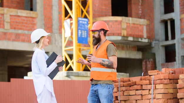 Relacionamentos entre clientes de construção e participantes da indústria da construção Conceito de comunicação da equipe de construção Mulher engenheira e construtor brutal comunicam o fundo do canteiro de obras