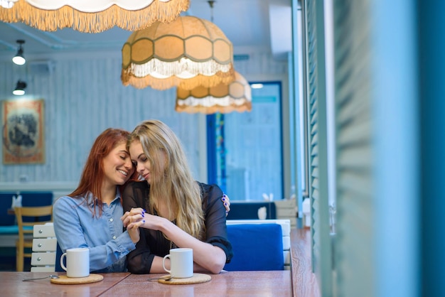 Relaciones del mismo sexo Feliz pareja lesbiana sentada en un café Las niñas se toman de la mano suavemente y beben café Abrazo de mujeres amorosas LGBT Dos mejores amigos en el café