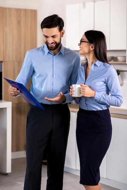 Relaciones positivas Alegres jóvenes colegas de negocios parados en la cocina mientras descansan después del trabajo