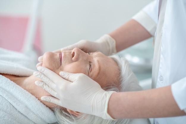 Relajación. Mujer madura de pelo gris acostado con los ojos cerrados con un masaje facial