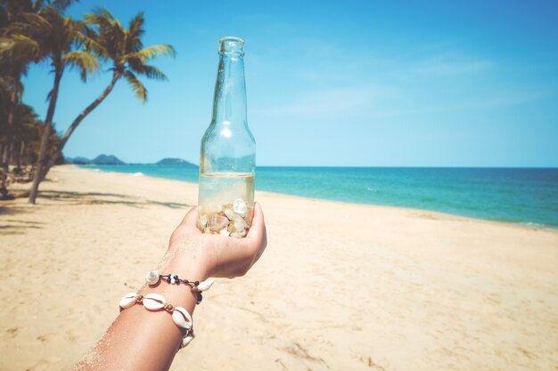 Relajación y Ocio en verano - Las mujeres jóvenes mano celebración botella con concha en la playa tropical en verano. efecto de tono de color vintage