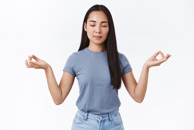 Relajación, paciencia y concepto de estilo de vida Atractiva joven asiática meditando reúne emociones positivas a través del ejercicio de yoga respirando levanta las manos de lado en posición de loto alcanzando el nirvana