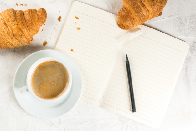 Relajación. Trabajo. Planificación de asuntos. Mesa de piedra blanca con un cuaderno para notas, estuches, tareas. Una taza de fragante café recién hecho. Croissants recién horneados. Lápiz. Copia espacio vista superior