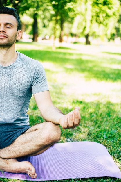Relajación de yoga masculino. Joven apuesto deportivo y delgado está haciendo ejercicios de yoga en el parque de la ciudad al aire libre. Estilo de vida saludable y alma y cuerpo fuertes