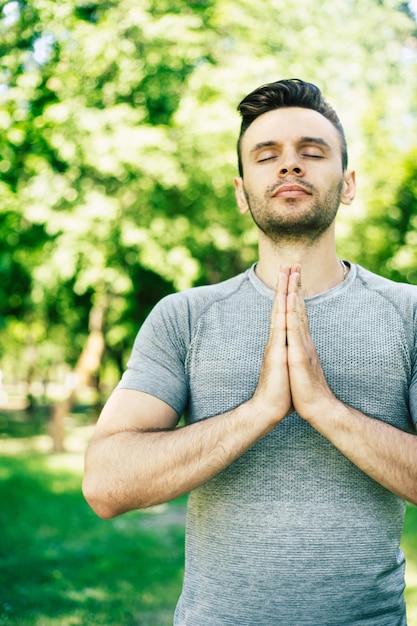 Relajación de yoga masculino. Joven apuesto deportivo y delgado está haciendo ejercicios de yoga en el parque de la ciudad al aire libre. Estilo de vida saludable y alma y cuerpo fuertes