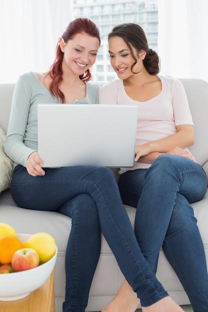 Relajado jóvenes amigas usando la computadora portátil en casa
