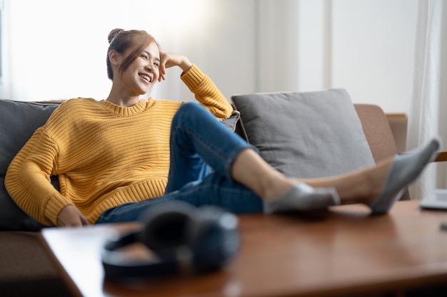 Relajante estilo de vida hogareño mujer asiática feliz en el sofá de la sala de relajación recostado con los brazos detrás de la cabeza sonriente chica asiática en un cómodo sillón de viaje viviendo